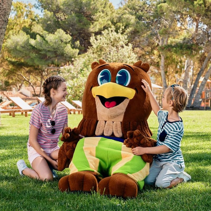 Two kids playing with a mascot outdoors at Falkensteiner Hotels