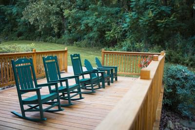 Series of rocking chairs on a wooden patio beside a forest