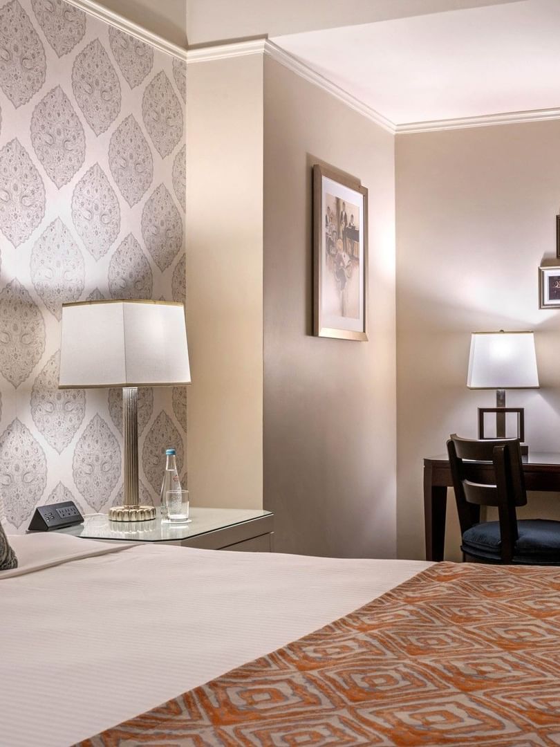 Patterned wallpaper with bed beside dark wood work desk with wall art in Premier room at Warwick New York 