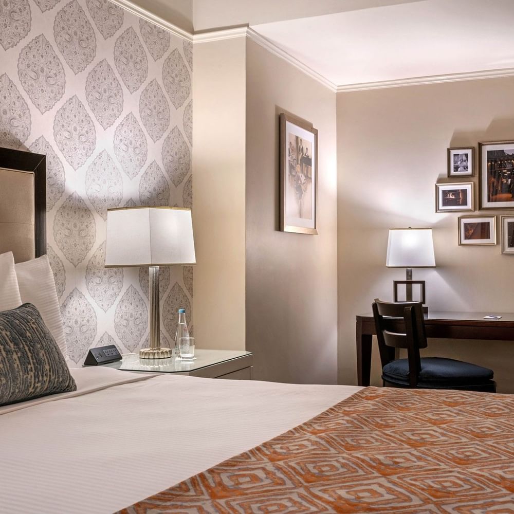 Patterned wallpaper with bed beside dark wood work desk with wall art in Premier room at Warwick New York 