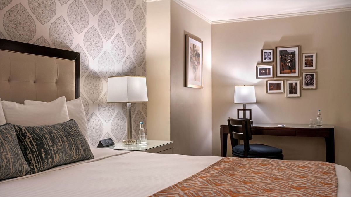 Patterned wallpaper with bed beside dark wood work desk with wall art in Premier room at Warwick New York 
