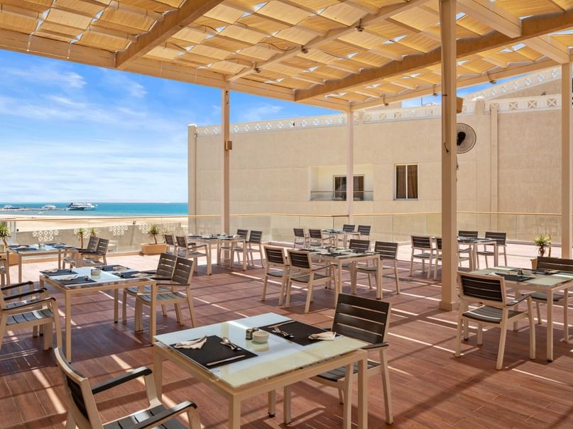 Terrassenrestaurant mit Blick auf das Meer, Holzdach und vielen Tischen und Stühlen.