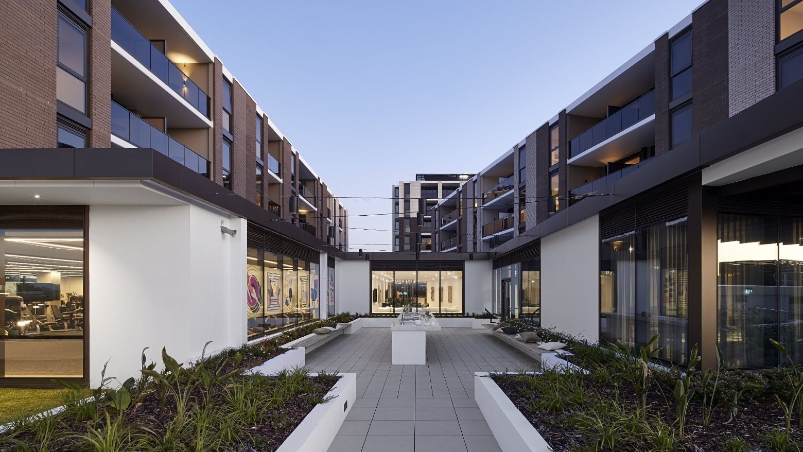 Exterior of a modern building with glass windows, balconies, and a landscaped courtyard area.