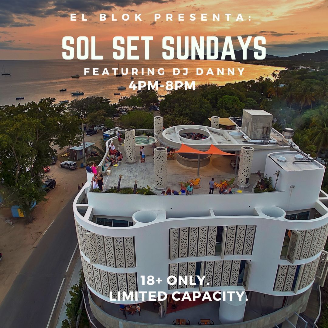 Aerial view of a modern white rooftop venue with guests gathered at sunset overlooking a tropical bay for Sol Set Sundays at El Blok Hotel.