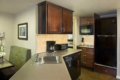 Fully equipped kitchenette with dark wood cabinets, stainless steel sink, and black appliances at London Bridge Resort