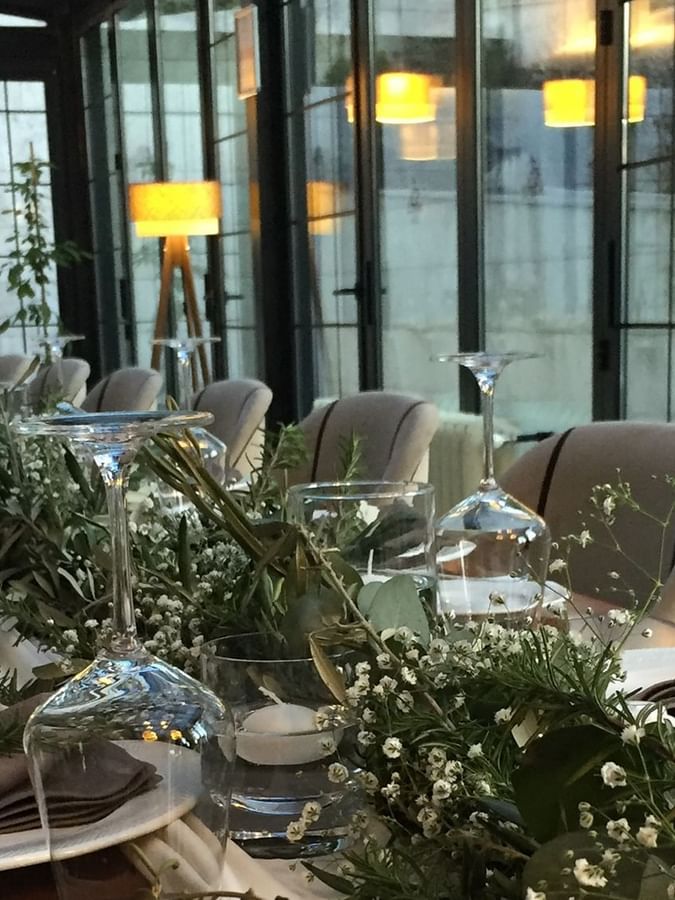 Long table with glasses by green plants surrounding a formal dinner setup in Maple Tree Restaurant at Warwick Ankara