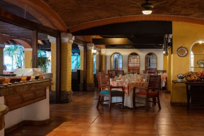 A restaurant with tiled floors, yellow walls, arched windows, and a buffet counter with various food items.