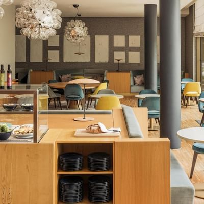 Modernes Restaurant mit bunten Stühlen, runden Tischen, Holztischen und Glasvitrinen mit Speisen.