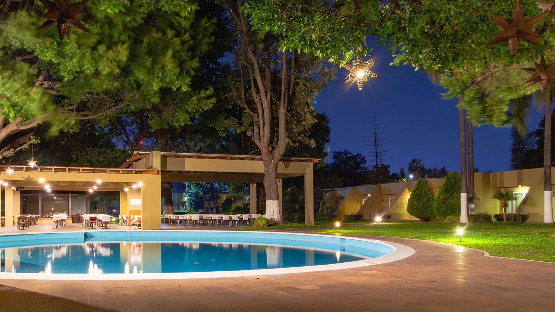 Outdoor night view of La Huerta restaurant featuring a pool, palm trees, and city light views  at Camino Real Guadalajara