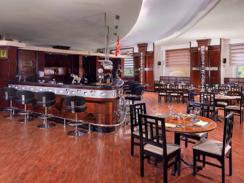 Elegant restaurant with wooden floors, bar counter, and dining tables with chairs, showcasing a sophisticated interior design.