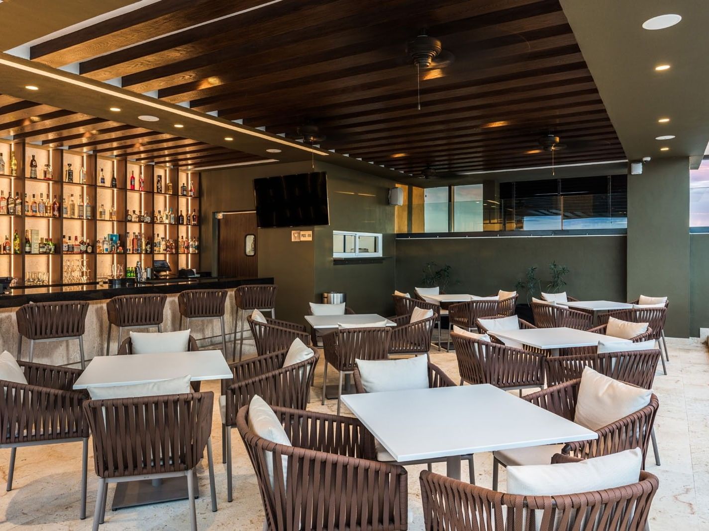 Stylish outdoor Blue Bar Merida with woven chairs, white tables, and a sunset sky view at Camino Real