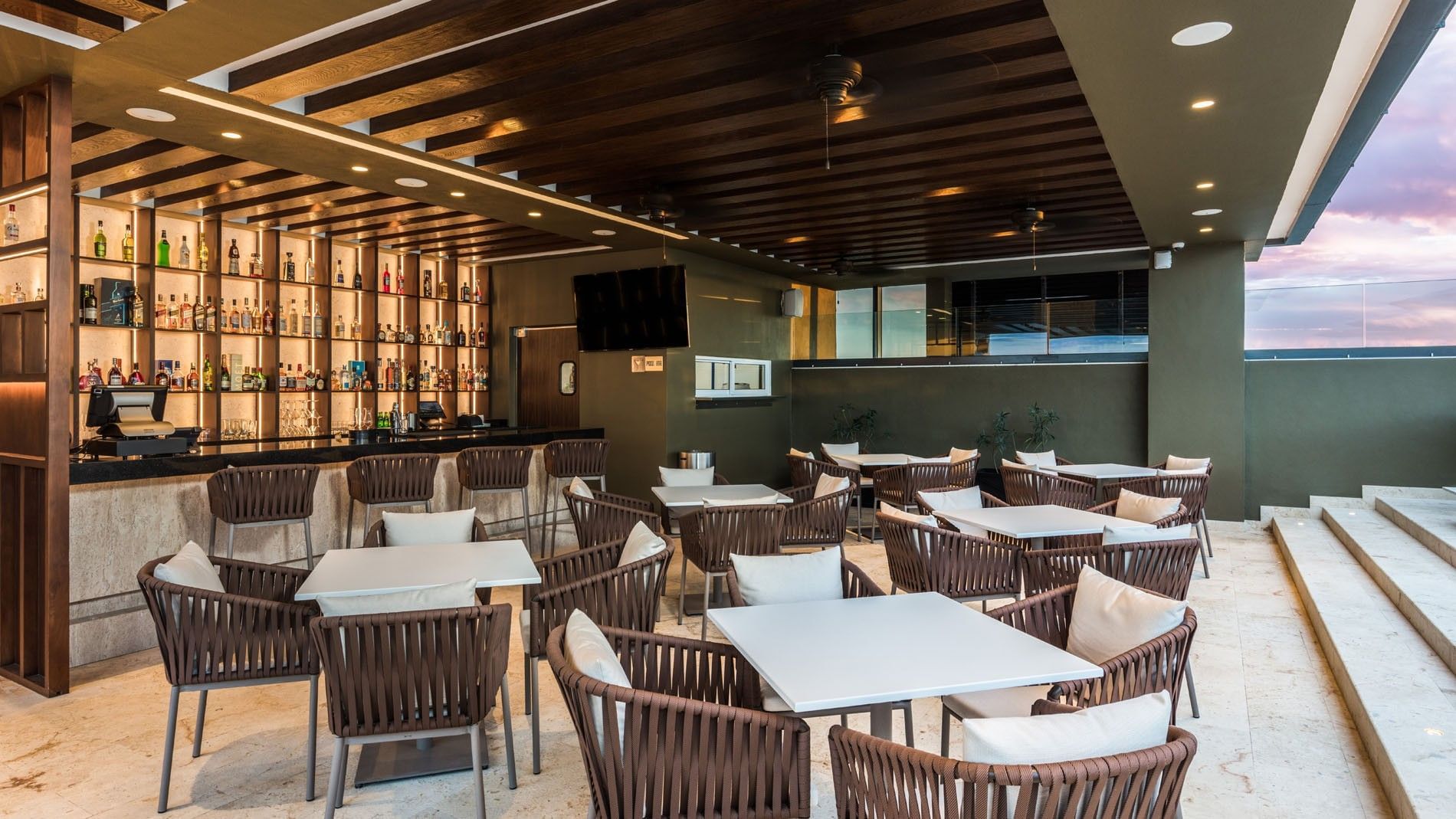 Stylish outdoor Blue Bar Merida with woven chairs, white tables, and a sunset sky view at Camino Real