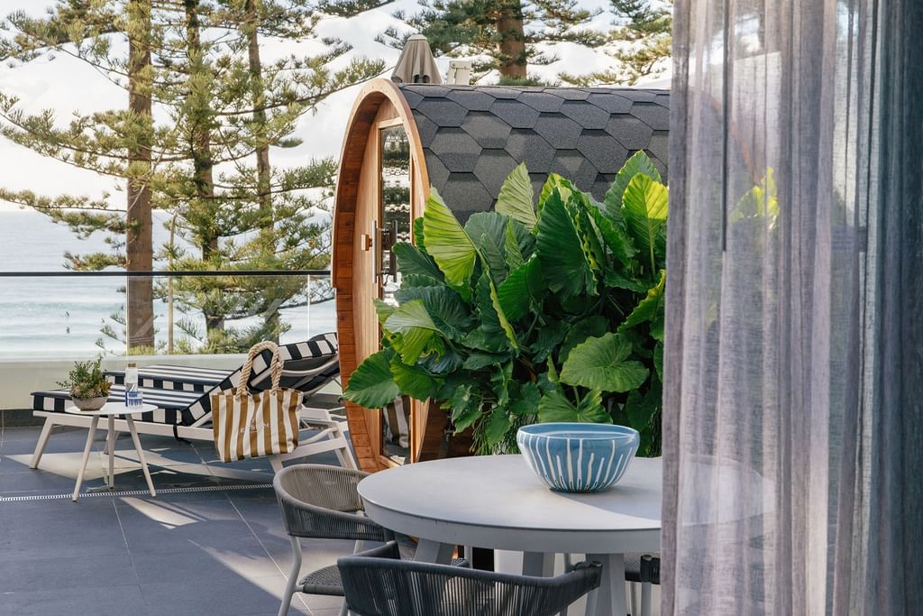 Outdoor terrace at Elysium Manly accommodation featuring a barrel sauna tucked among leafy plants beside a dining table