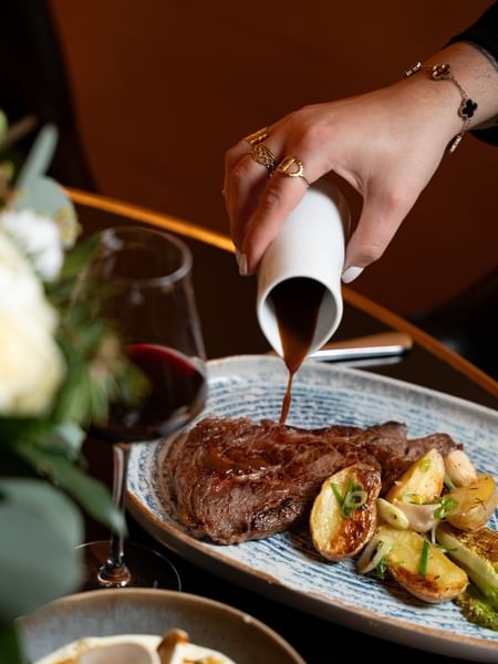 Guest pouring sauce from a white pitcher by a wine glass in Restaurant “Le W”at Warwick Paris Champs Elysées