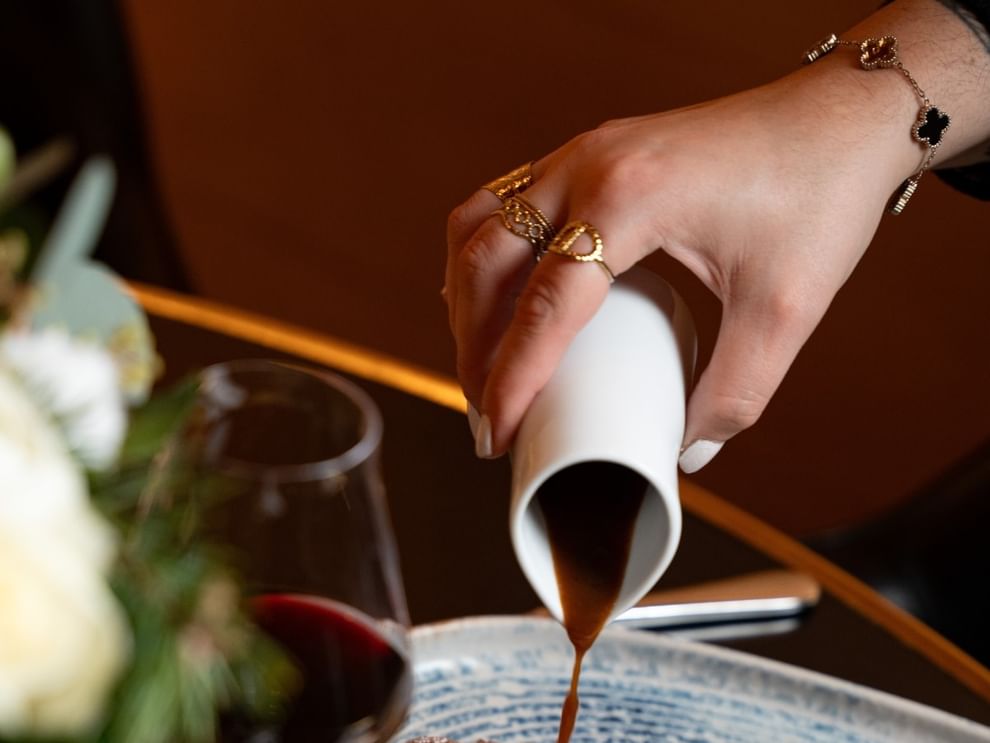 Guest pouring sauce from a white pitcher by a wine glass in Restaurant “Le W”at Warwick Paris Champs Elysées