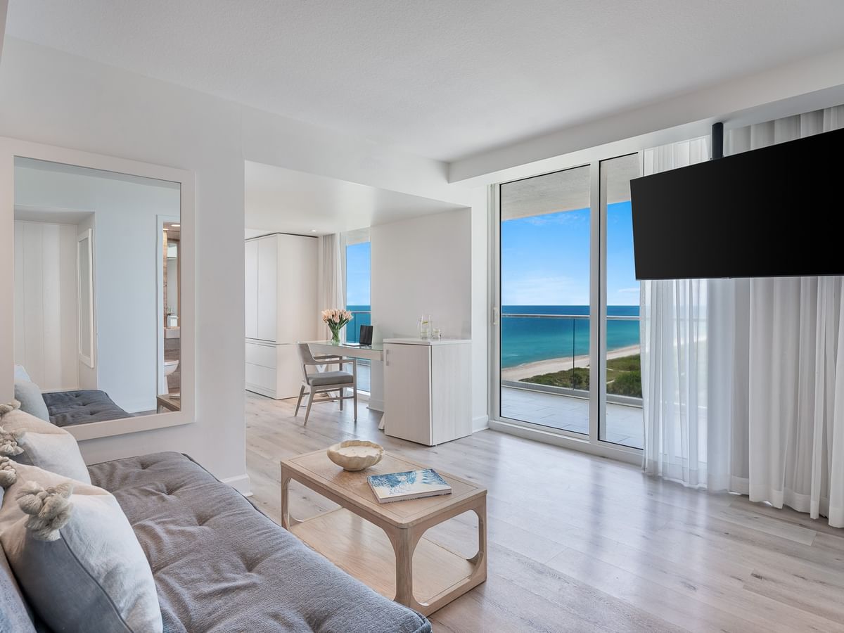 Living area with couch facing mounted TV & ocean balcony in King Ocean Front Corner Suites at Grand Beach Hotel Surfside