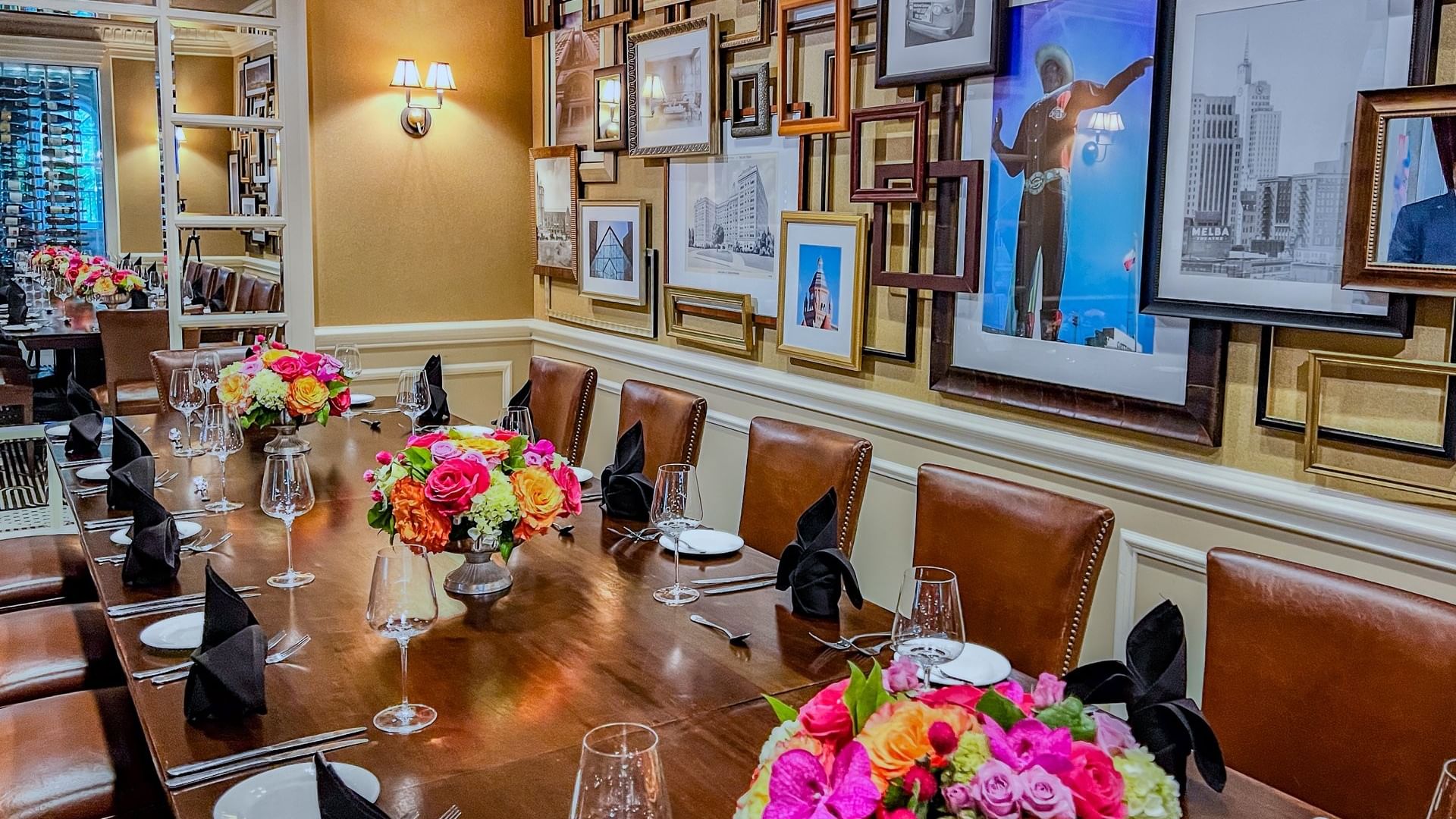 Floral bouquets on a wooden table by leather chairs under a gallery wall in Private Dining at Warwick Melrose Dallas