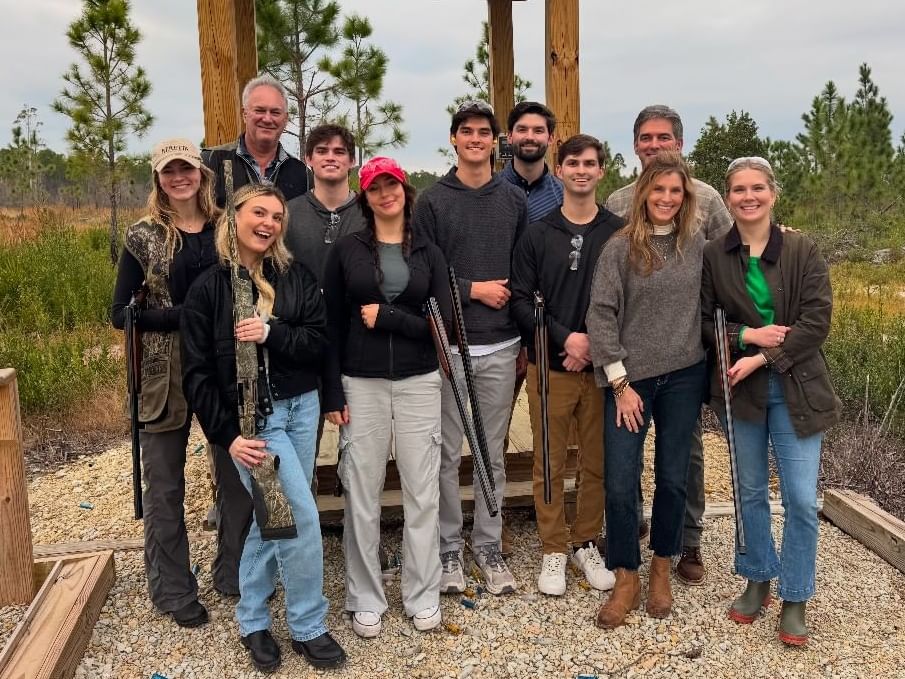 Group of people standing together with shotguns, smiling for the camera in an outdoor setting.