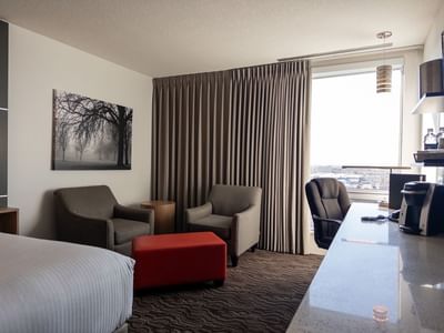 Hotel room with bed, chairs, desk, and window at Carriage House Hotel & Conference Centre.