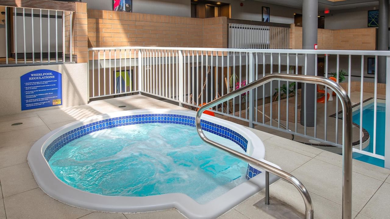 Indoor whirlpool with blue mosaic tile trim and metal handrail at Coast Calgary University Area Hotel by APA.