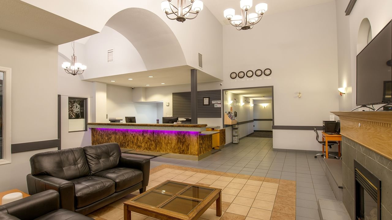Reception area with black leather couches, glass table, and a fireplace with mounted TV.