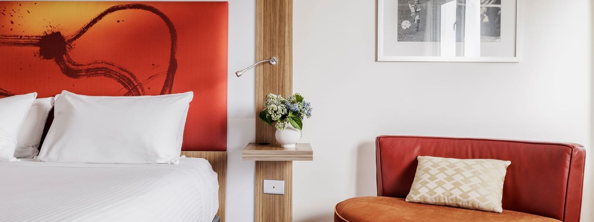 Comfy seating area by the plush king bed with vibrant orange artwork in Superior Room at Novotel Sydney Olympic Park