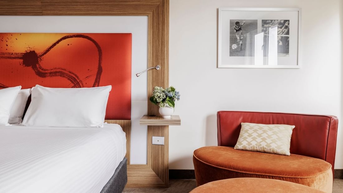 Comfy seating area by the plush king bed with vibrant orange artwork in Superior Room at Novotel Sydney Olympic Park