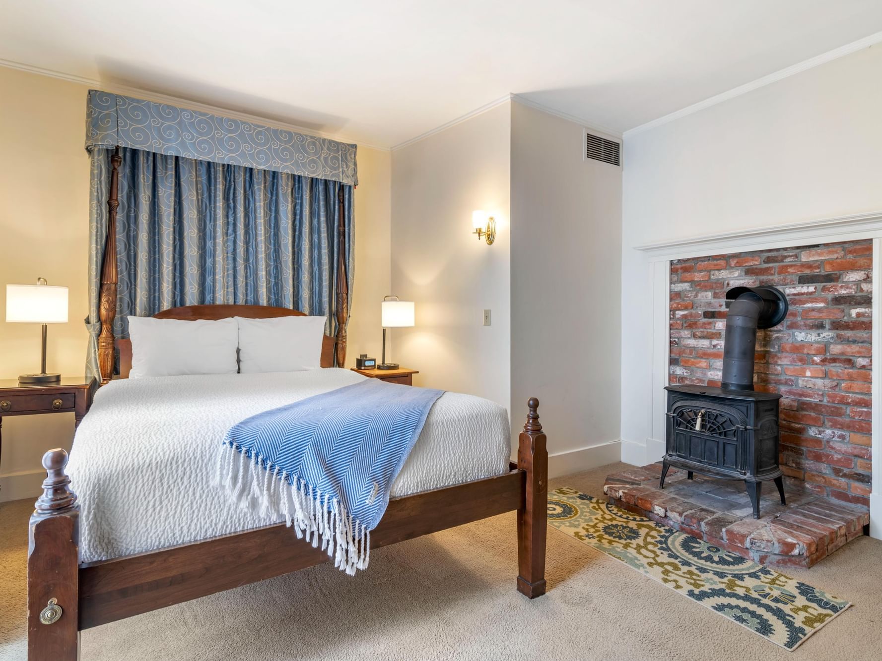 Cozy bedroom with a fireplace, bedside lamps & queen bed in Deluxe Room at Harraseeket Inn