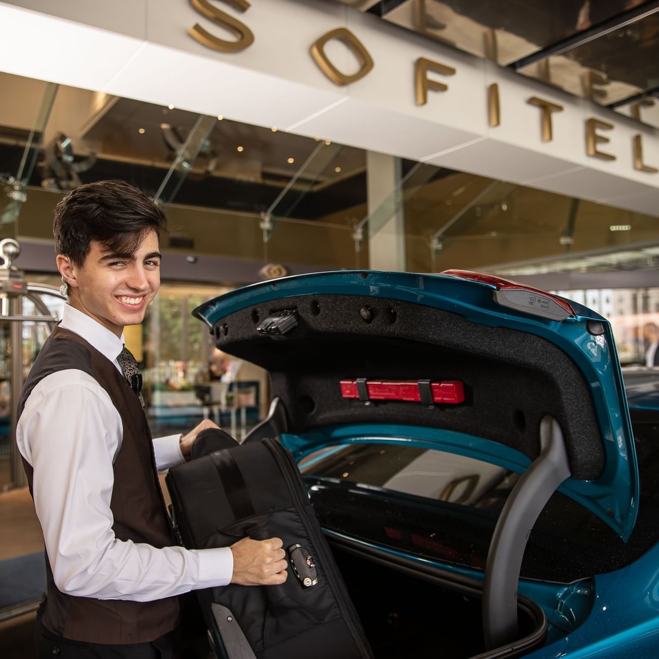 A bellboy stands beside a car and holding a suitcase at Sofitel Brisbane Central