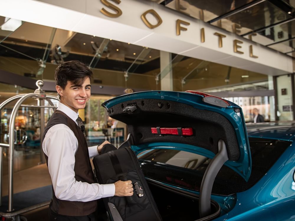 A bellboy stands beside a car and holding a suitcase at Sofitel Brisbane Central