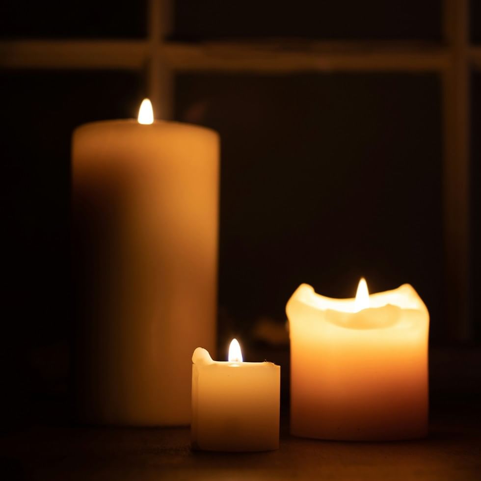 Three lit candles of varying sizes on a dark surface with a window in the background.