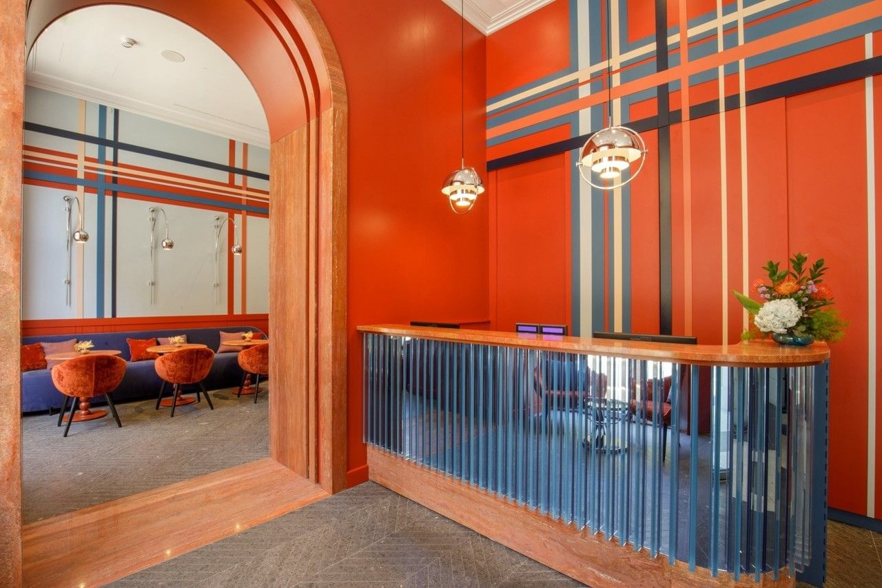 Lobby of the Independent Hotel in Rome with vibrant red-orange walls, modern striped wall design, stylish seating, a curved reception desk, and large plants creating a welcoming atmosphere.