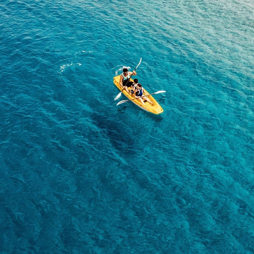 Tre persone in un kayak giallo con pagaie, su acque blu in un giorno di sole.