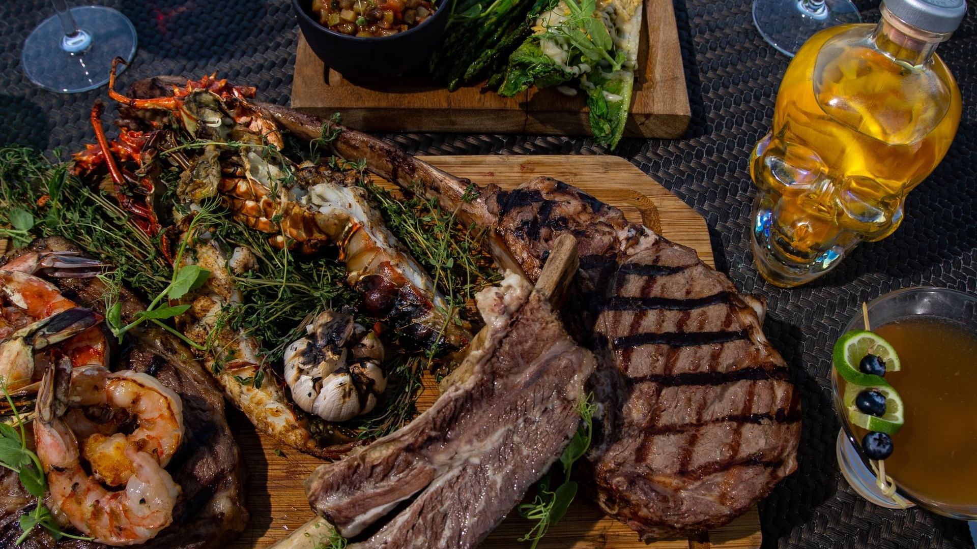 Plato de filete tomahawk a la parrilla y langosta junto a una botella de calavera en De Cortez Grill House, Hacienda Del Mar, Los Cabos.
