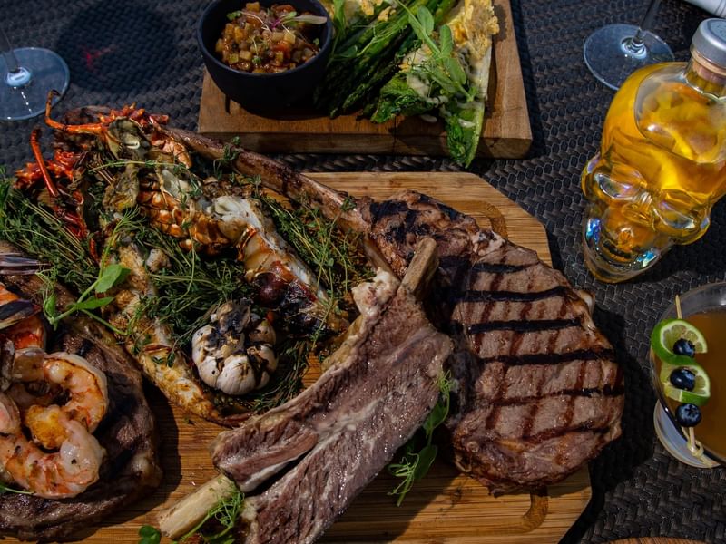 Close-up of Tomahawk steak and grilled seafood platter on a wooden board at Hacienda Del Mar Los Cabos