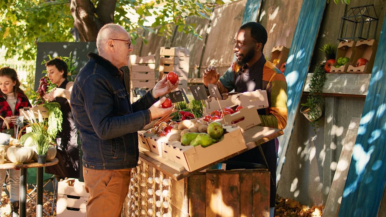 Man examining fresh tomatoes while interacting with a vendor at Penticton Farmers’ Market near Coast Penticton Hotel