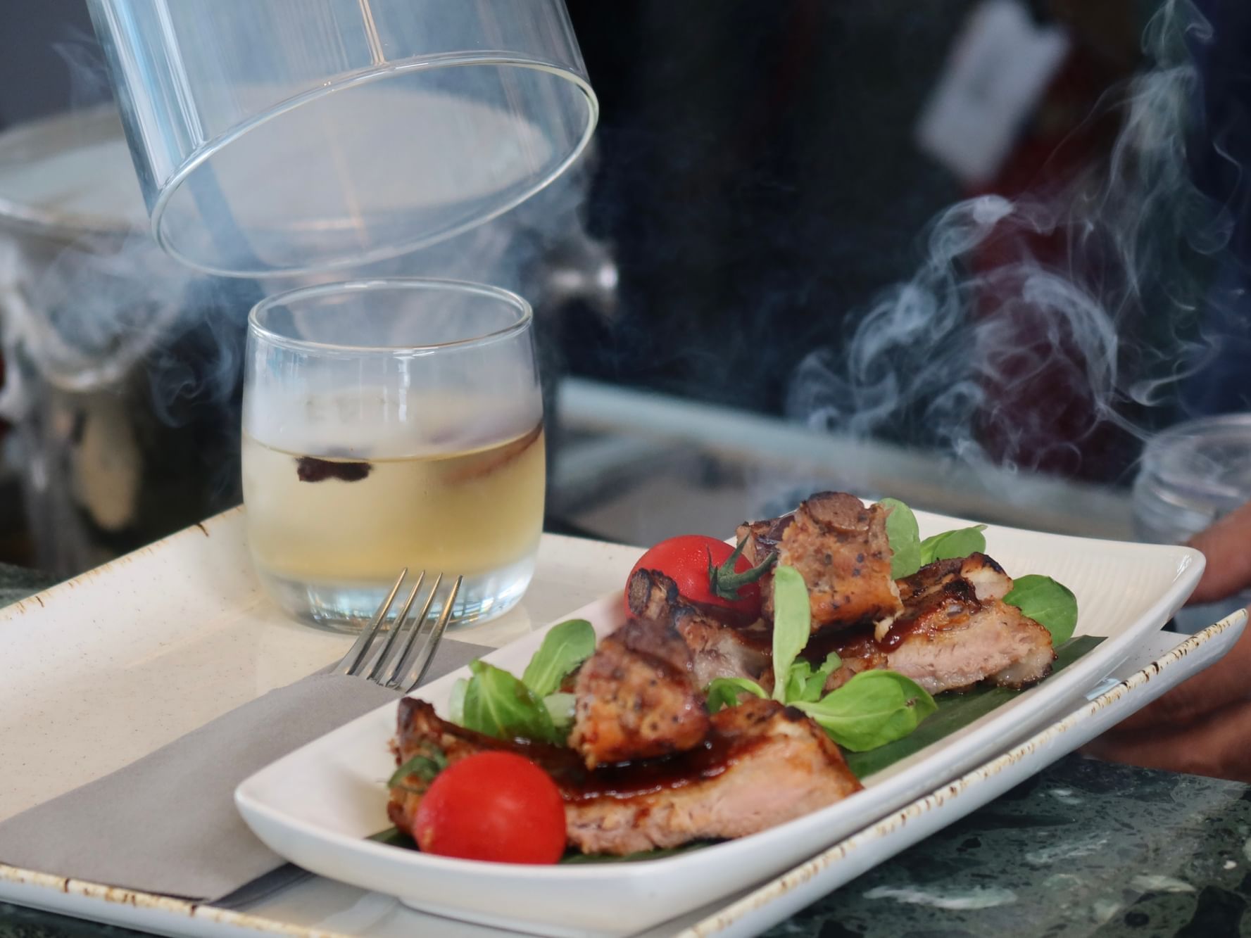 A smoked cocktail with a grilled pork chop main course served on a long white plate at Momentus Hotel Alexandra
