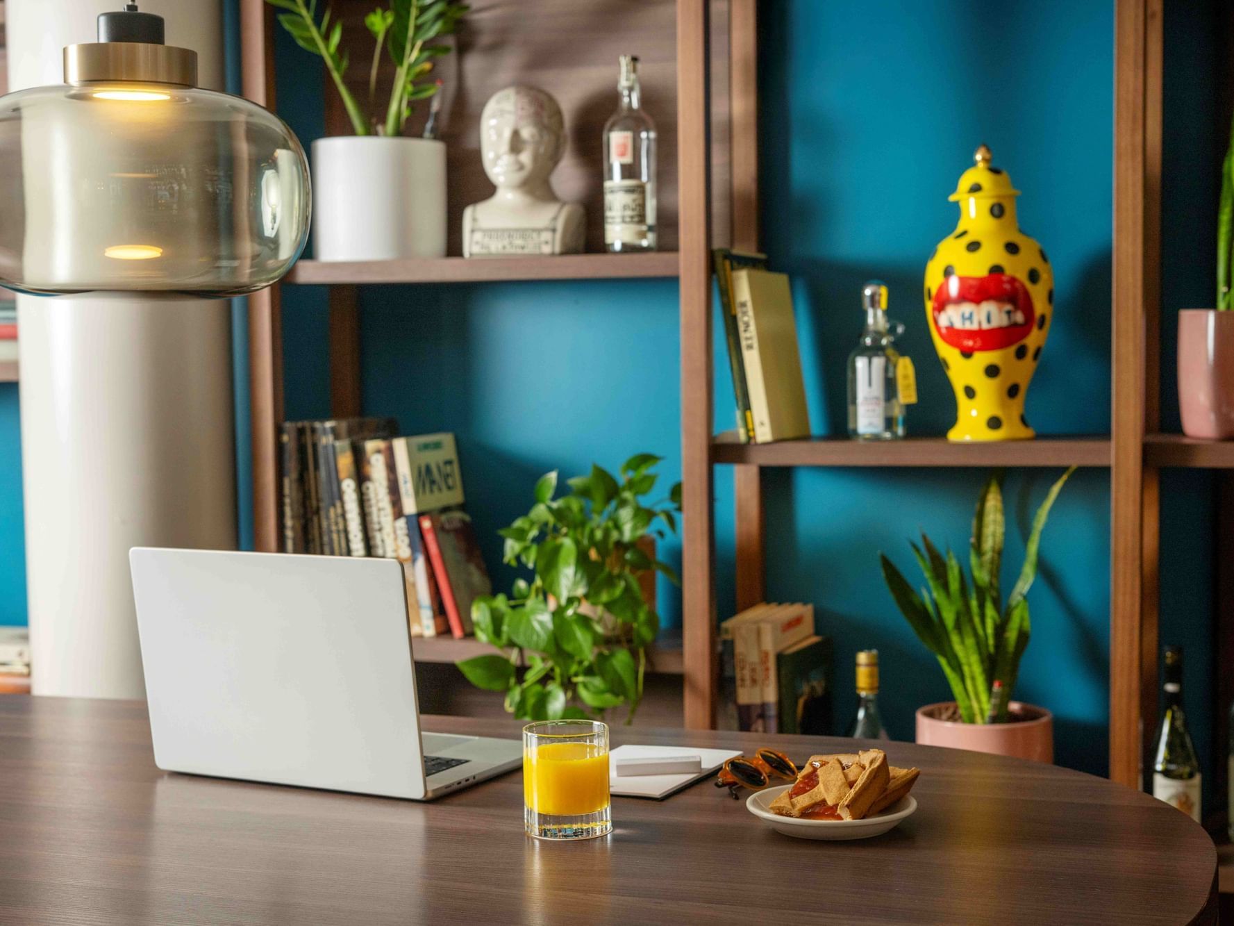 Modern workspace with a laptop, juice, and colorful shelving on a dark desk at Urban Hive Milano