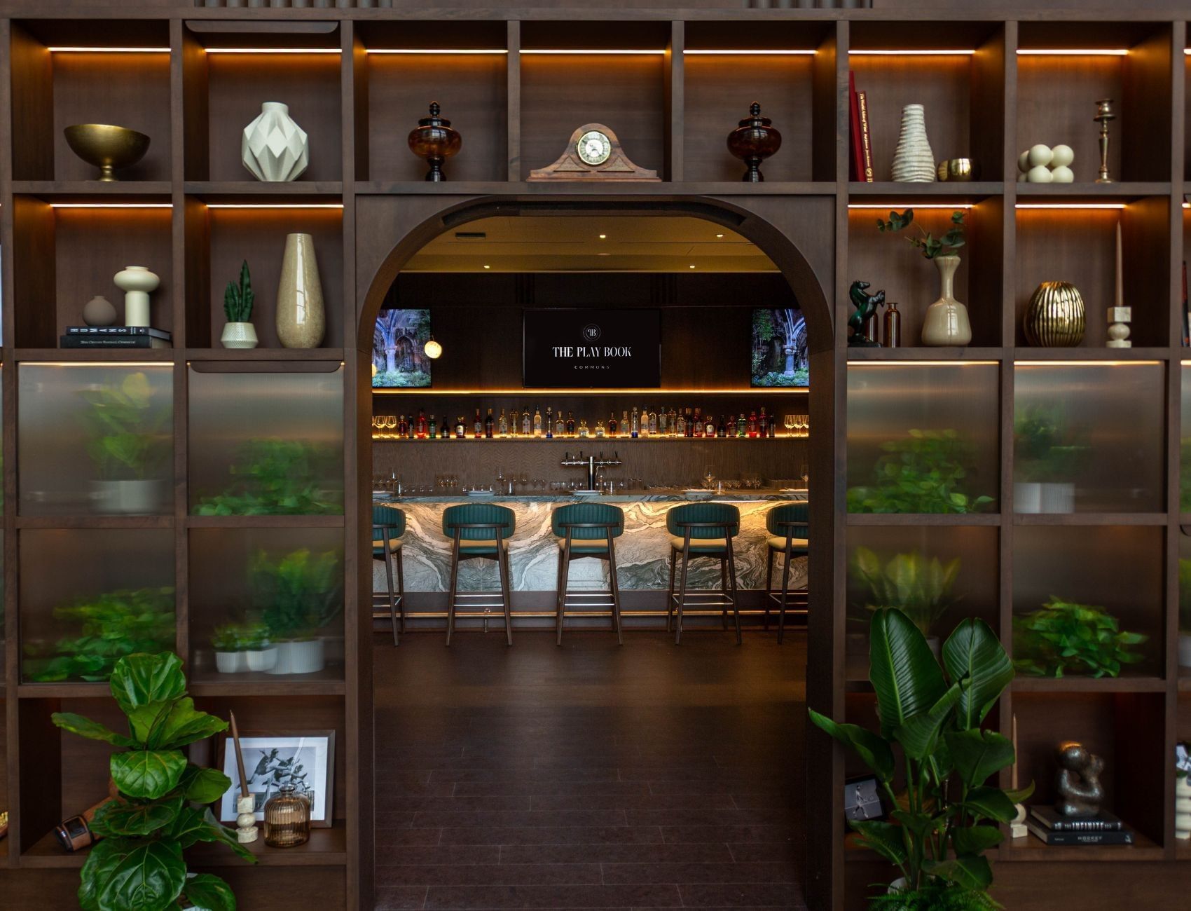 Hotel Bar at Hotel X Toronto, with green stools placed by a marble counter under an arched, plant-filled doorway