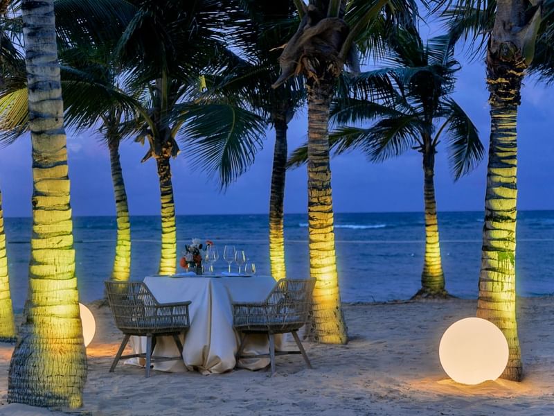 Beachside table next to palm trees & illuminated lighting at Live Aqua Punta Cana