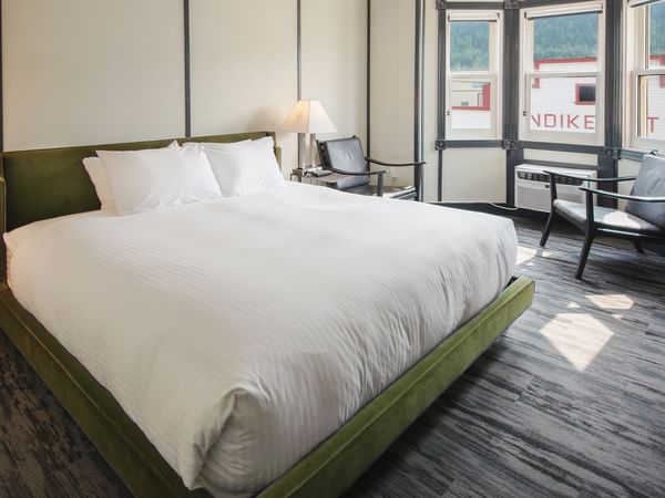 Hotel room with king bed, lamp, night stand, chair, and window