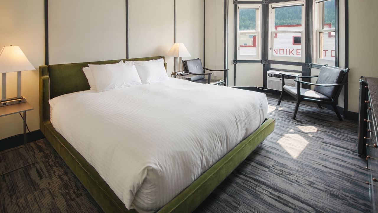 Hotel room with king bed, lamp, night stand, chair, and window