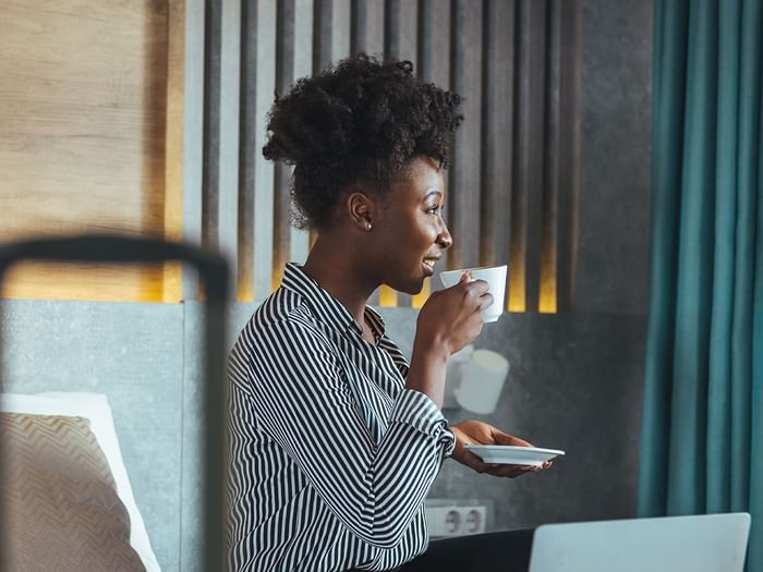 Women drinking coffee on a hotel room bed with laptop open