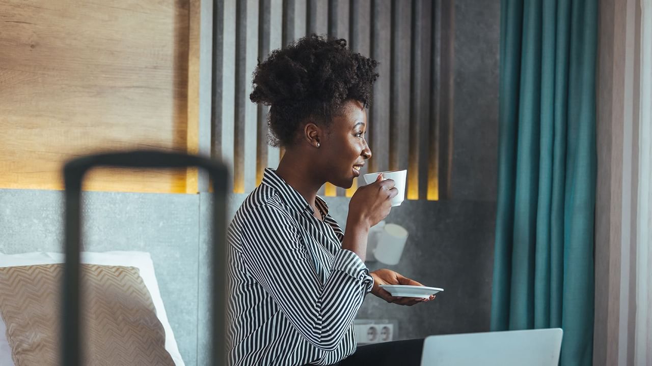 Women drinking coffee on a hotel room bed with laptop open