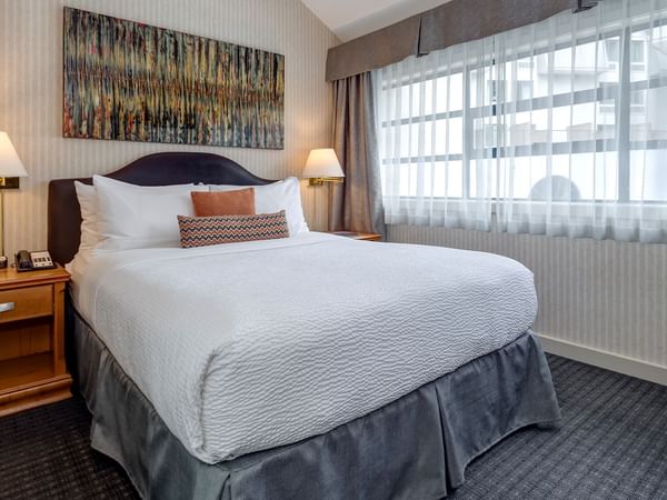 A hotel room with a large bed, two nightstands, two lamps, and a window with curtains.