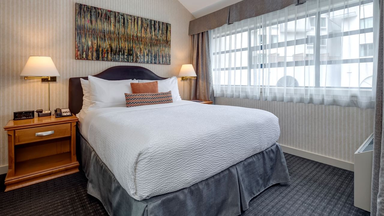 A hotel room with a large bed, two nightstands, two lamps, and a window with curtains.