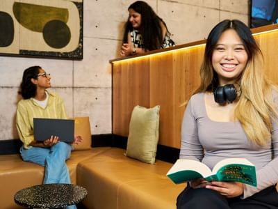 A resident with headphones reads a book while other women use their laptops nearby.