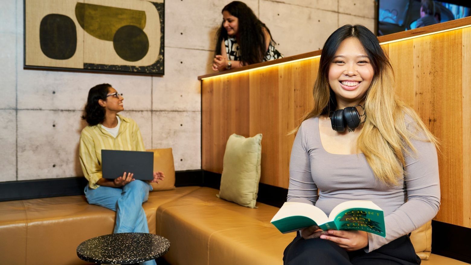 A resident with headphones reads a book while other women use their laptops nearby.