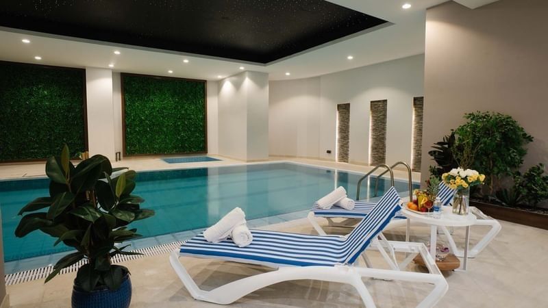 Striped lounge chairs with towels by an indoor pool under a black ceiling at Cantonal Hotel by Warwick Riyadh