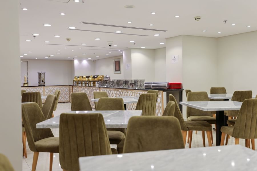 Dining area featuring marble tables with olive green chairs, and buffet setup at Saja by Warwick Makkah